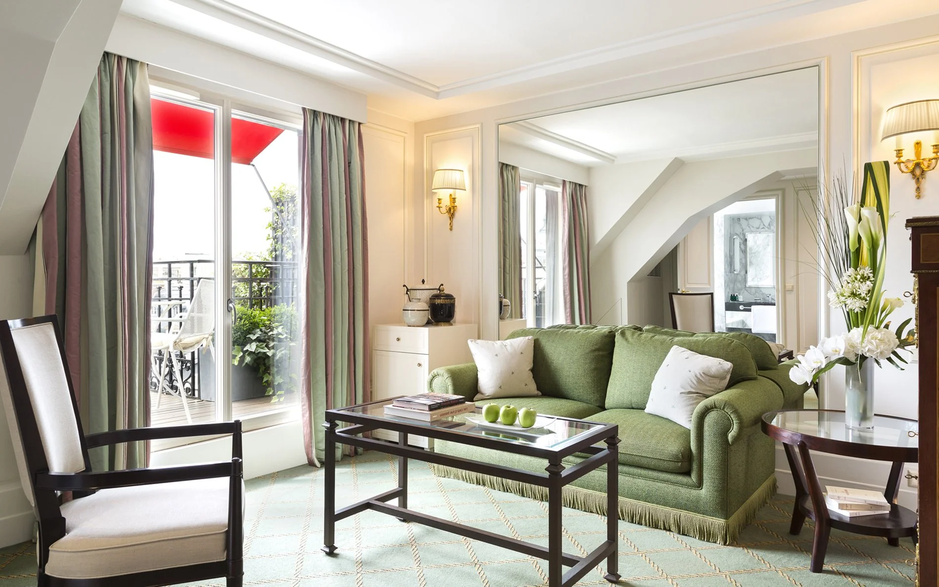 Salon élégant de la Terrace Junior Suite de l’Hôtel San Régis, avec canapé vert et miroir pleine hauteur.